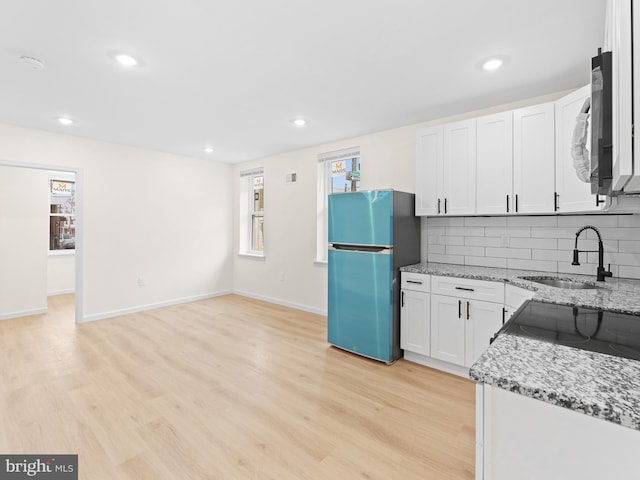 kitchen with white cabinetry, sink, light stone countertops, stainless steel fridge, and decorative backsplash