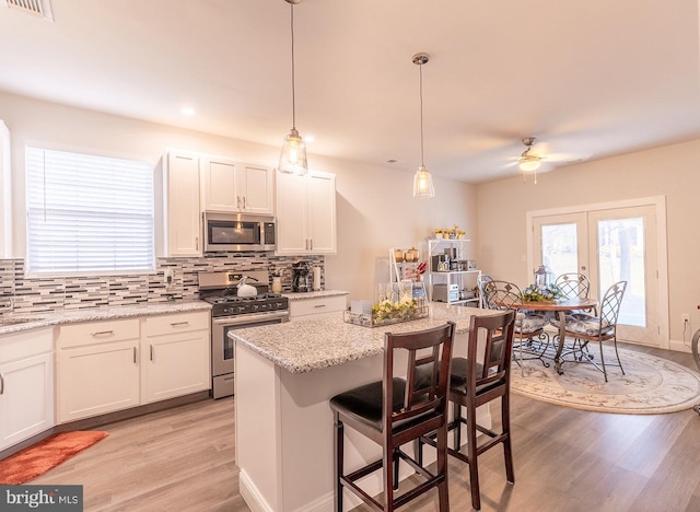 kitchen featuring hanging light fixtures, ceiling fan, light stone countertops, white cabinetry, and stainless steel appliances