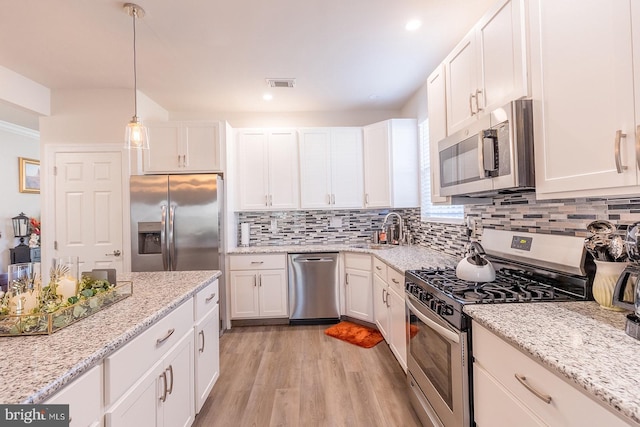 kitchen with appliances with stainless steel finishes, light stone counters, sink, decorative light fixtures, and white cabinets