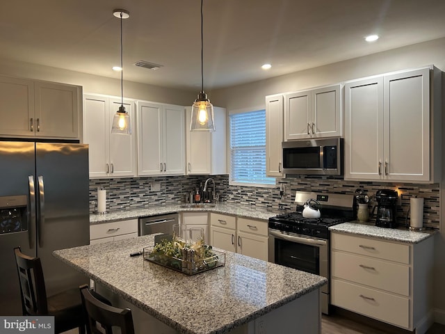 kitchen featuring tasteful backsplash, light stone counters, a kitchen island, and appliances with stainless steel finishes