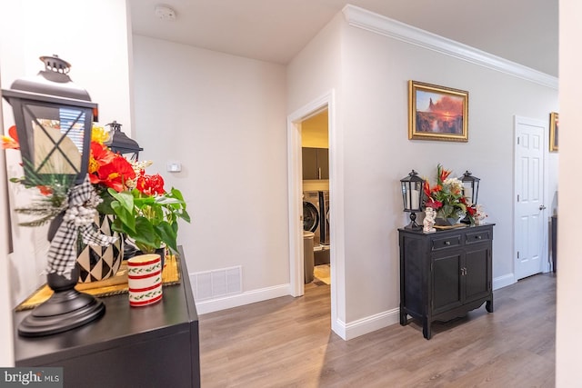 hallway with washer and clothes dryer, wood-type flooring, and ornamental molding