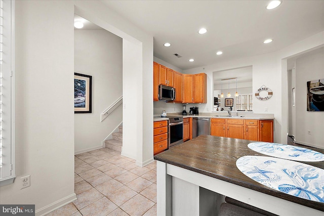 kitchen with kitchen peninsula, appliances with stainless steel finishes, sink, light tile patterned floors, and decorative light fixtures