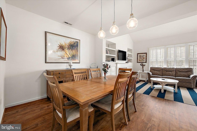 dining area featuring built in shelves, dark wood-type flooring, and vaulted ceiling