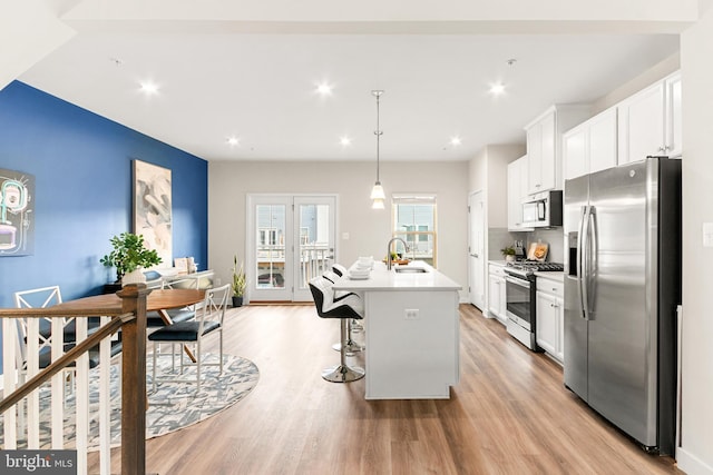 kitchen featuring white cabinetry, sink, hanging light fixtures, stainless steel appliances, and an island with sink