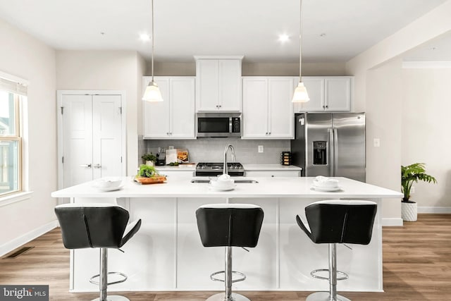 kitchen featuring sink, an island with sink, decorative light fixtures, white cabinetry, and stainless steel appliances