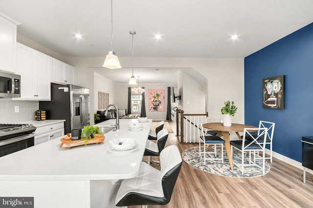 kitchen with sink, tasteful backsplash, an island with sink, decorative light fixtures, and white cabinets