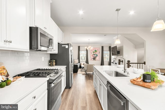 kitchen with stainless steel appliances, sink, decorative light fixtures, white cabinets, and a chandelier