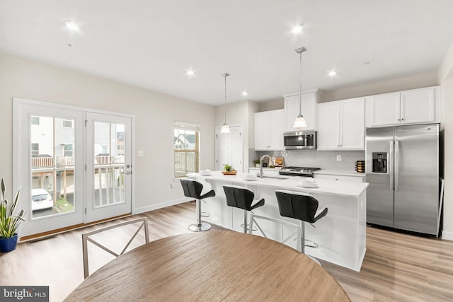 kitchen featuring decorative backsplash, stainless steel appliances, a center island with sink, white cabinetry, and hanging light fixtures