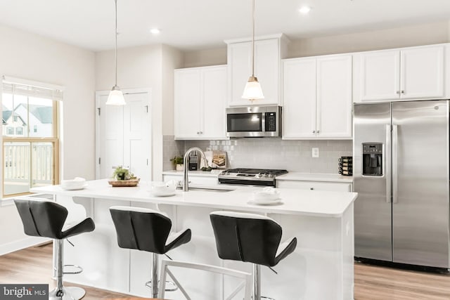 kitchen featuring decorative light fixtures, sink, stainless steel appliances, and a kitchen island with sink