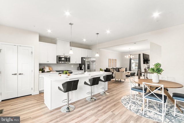 kitchen with pendant lighting, white cabinets, an island with sink, stainless steel appliances, and a chandelier