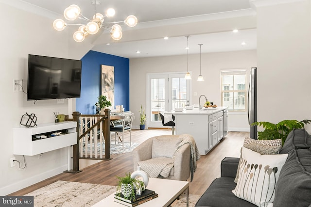 living room featuring a chandelier, light wood-type flooring, crown molding, and sink