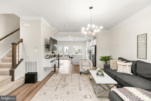 living room with french doors, light wood-type flooring, ornamental molding, sink, and a notable chandelier