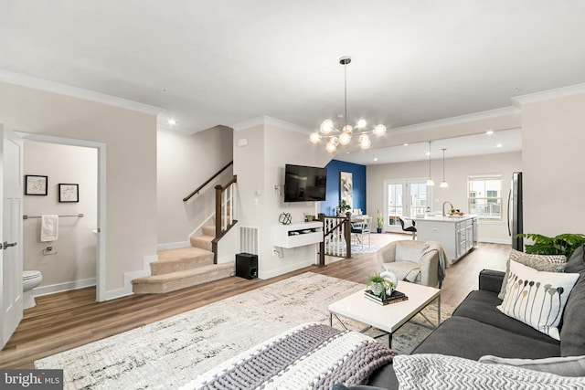 living room with light hardwood / wood-style floors, an inviting chandelier, crown molding, and sink