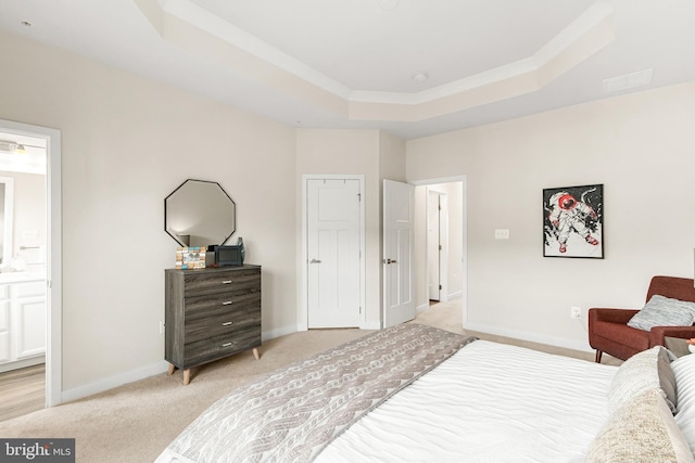 bedroom featuring a raised ceiling, light colored carpet, and ensuite bath