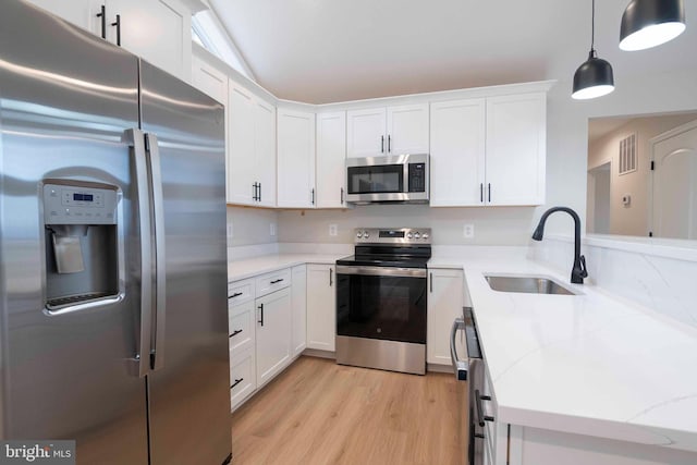 kitchen with light wood-type flooring, stainless steel appliances, sink, white cabinetry, and hanging light fixtures