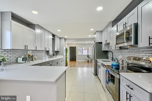 kitchen with sink, light tile patterned floors, appliances with stainless steel finishes, tasteful backsplash, and kitchen peninsula