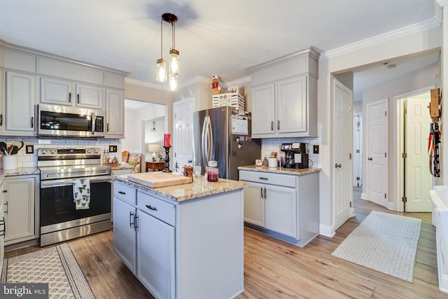 kitchen with appliances with stainless steel finishes, backsplash, light hardwood / wood-style floors, a kitchen island, and hanging light fixtures