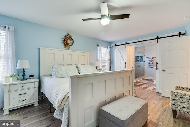 bedroom featuring hardwood / wood-style flooring, ceiling fan, and a barn door