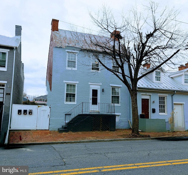 view of front of house with metal roof, brick siding, a chimney, and a standing seam roof