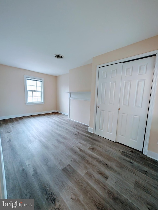 unfurnished bedroom with a closet, visible vents, baseboards, and wood finished floors