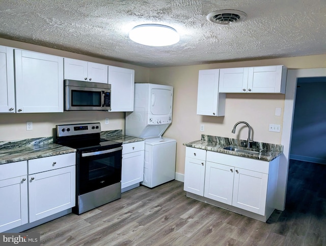 kitchen with stainless steel appliances, sink, light hardwood / wood-style floors, white cabinetry, and stacked washer / drying machine