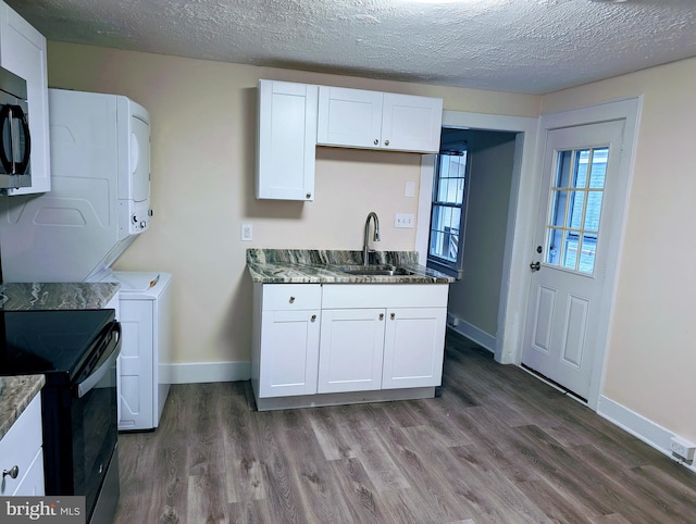 kitchen featuring sink, white cabinetry, and stacked washer / dryer