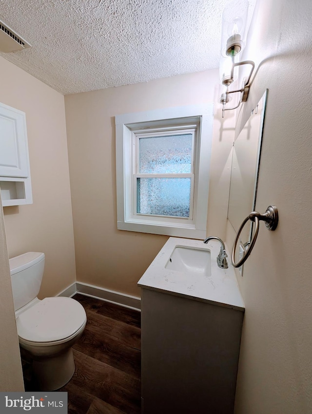 half bathroom featuring visible vents, toilet, a textured ceiling, wood finished floors, and vanity