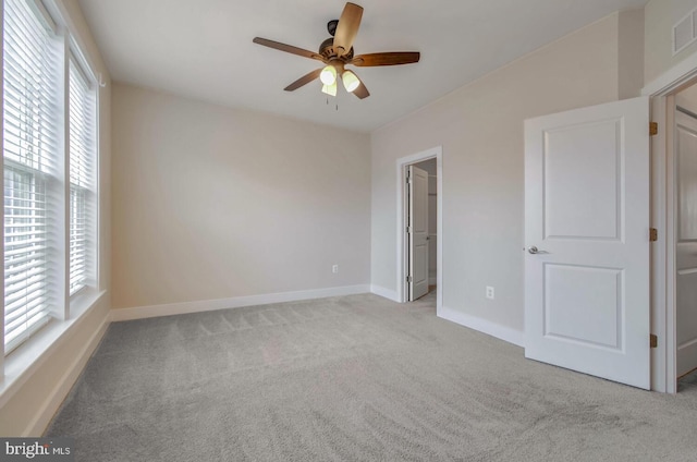 interior space featuring ceiling fan, a walk in closet, multiple windows, and light carpet