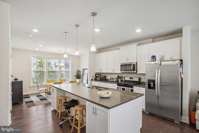 kitchen featuring stainless steel appliances, sink, white cabinets, hanging light fixtures, and a center island with sink