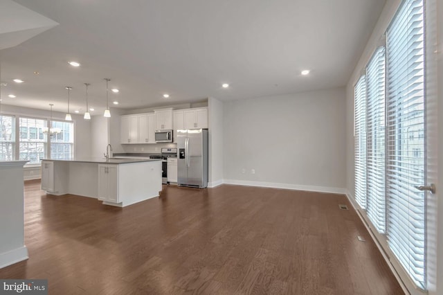 kitchen with appliances with stainless steel finishes, hanging light fixtures, an island with sink, and white cabinets