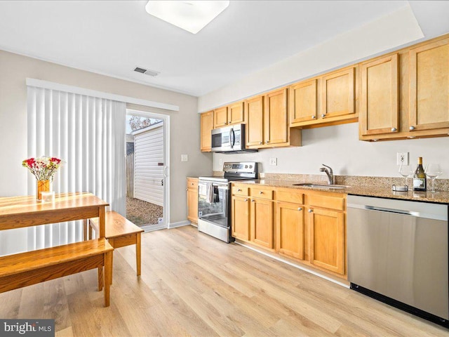 kitchen with light stone counters, sink, stainless steel appliances, and light hardwood / wood-style flooring