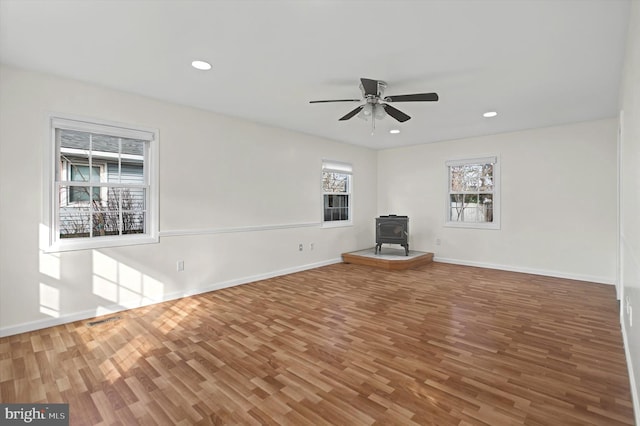 unfurnished living room with hardwood / wood-style floors, a wood stove, and ceiling fan