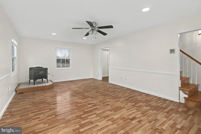 unfurnished living room with ceiling fan, light wood-type flooring, and a wood stove