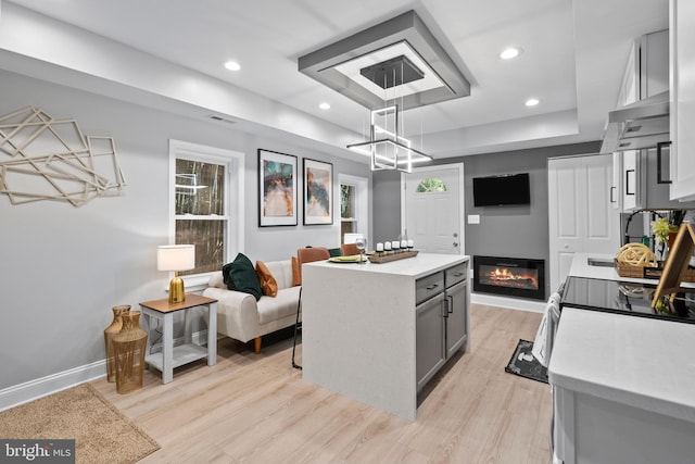 kitchen with gray cabinetry, light hardwood / wood-style floors, a kitchen island, hanging light fixtures, and range hood