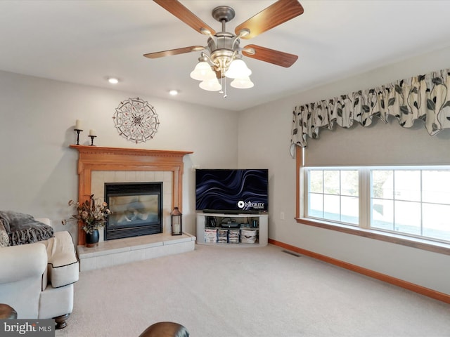 carpeted living room featuring ceiling fan and a tiled fireplace