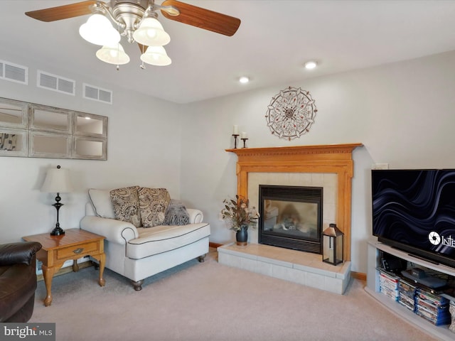 carpeted living room with ceiling fan and a tiled fireplace