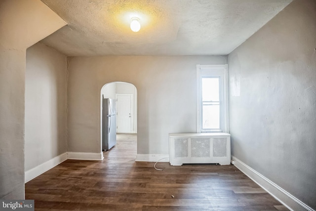 unfurnished room featuring a textured ceiling, radiator heating unit, and dark wood-type flooring