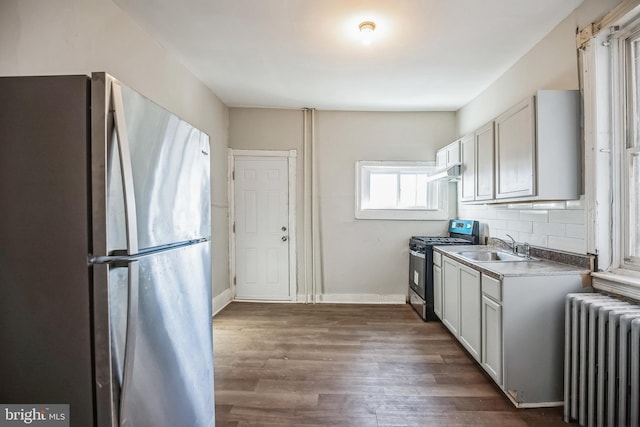 kitchen featuring radiator, sink, dark hardwood / wood-style floors, appliances with stainless steel finishes, and tasteful backsplash