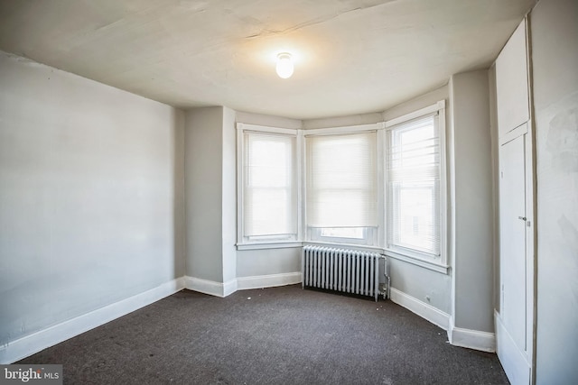 empty room with dark colored carpet, a wealth of natural light, and radiator