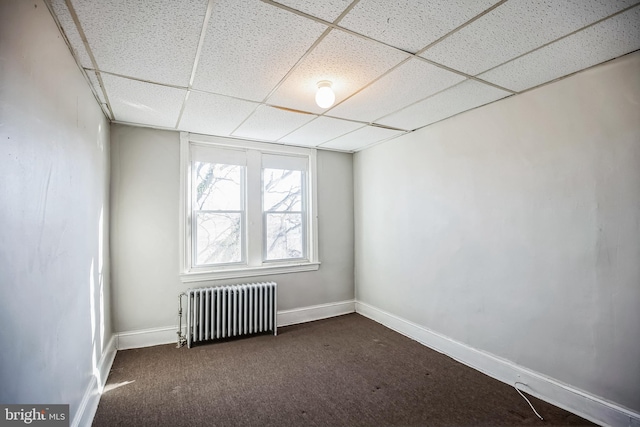 empty room featuring radiator, a paneled ceiling, and dark carpet