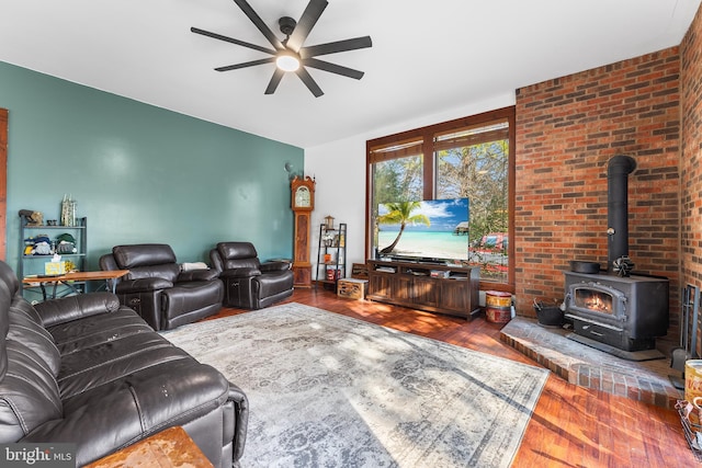 living room featuring a wood stove, ceiling fan, hardwood / wood-style floors, and brick wall