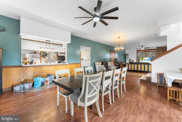 dining space with hardwood / wood-style floors, ceiling fan with notable chandelier, and wooden walls