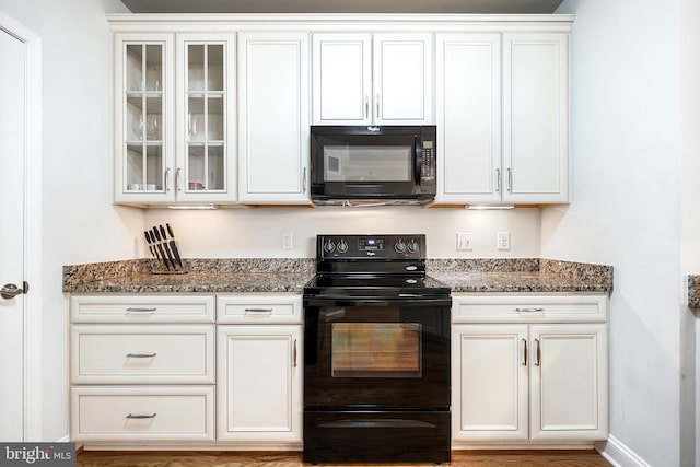 kitchen featuring white cabinets, hardwood / wood-style floors, dark stone counters, and black appliances