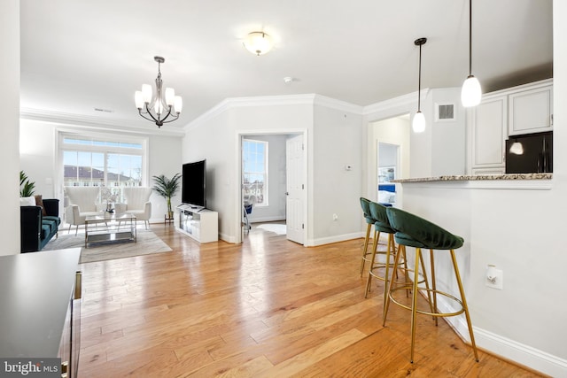 kitchen with black fridge, light stone countertops, light wood-type flooring, ornamental molding, and white cabinetry