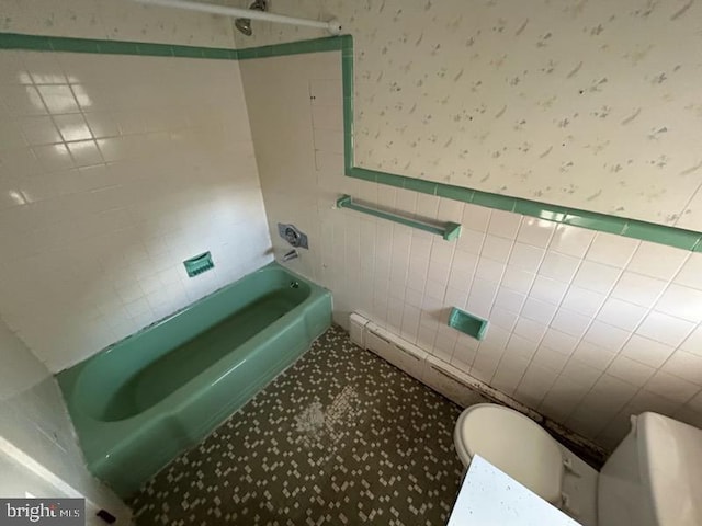 bathroom featuring toilet, tile walls, and tiled shower / bath