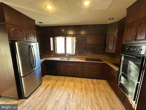 kitchen with black appliances, dark brown cabinets, light wood-type flooring, and sink