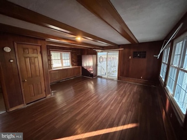 unfurnished living room featuring wooden walls, dark hardwood / wood-style flooring, and beamed ceiling