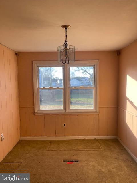 unfurnished dining area with wooden walls, carpet floors, and a chandelier