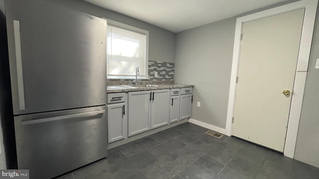 kitchen featuring decorative backsplash, white cabinetry, sink, and stainless steel refrigerator