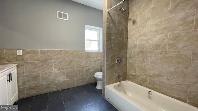 full bathroom featuring vanity, toilet, tile walls, and tiled shower / bath combo